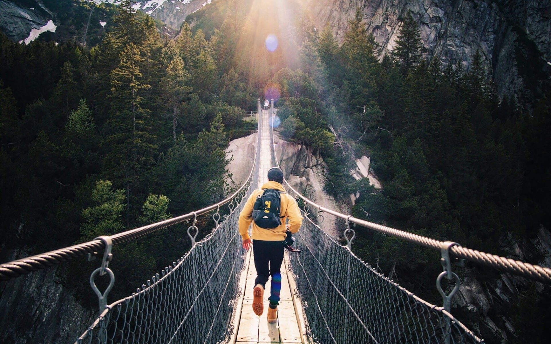 Person crossing a suspension bridge in the mountains, symbolizing adventure travel