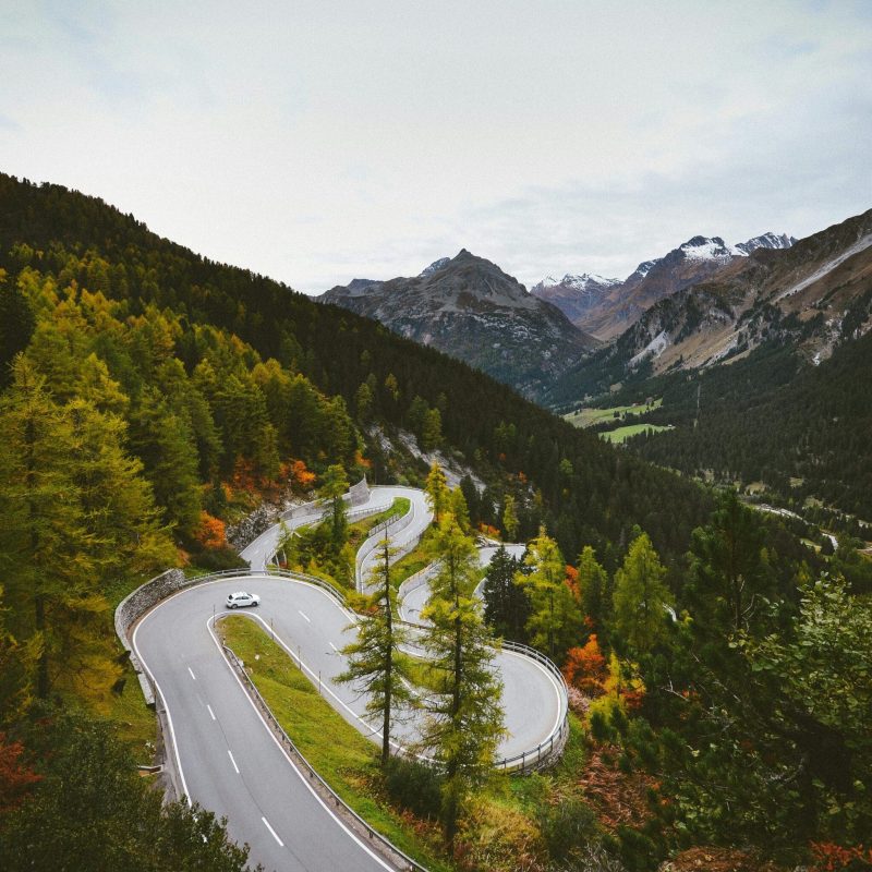 A winding mountain road surrounded by lush autumn foliage and distant snow-capped peaks