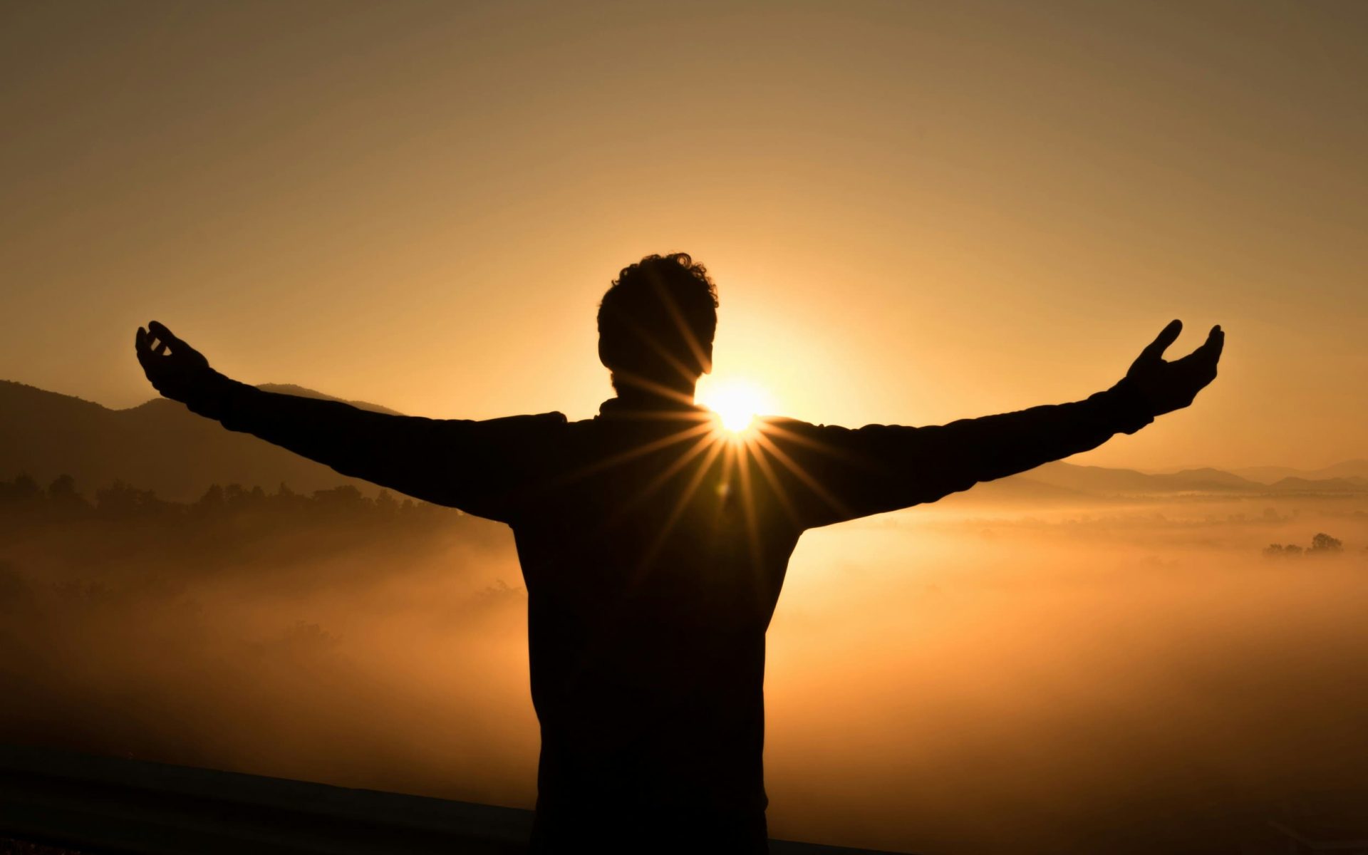 Person with outstretched arms at sunrise, symbolizing self-care and mindfulness