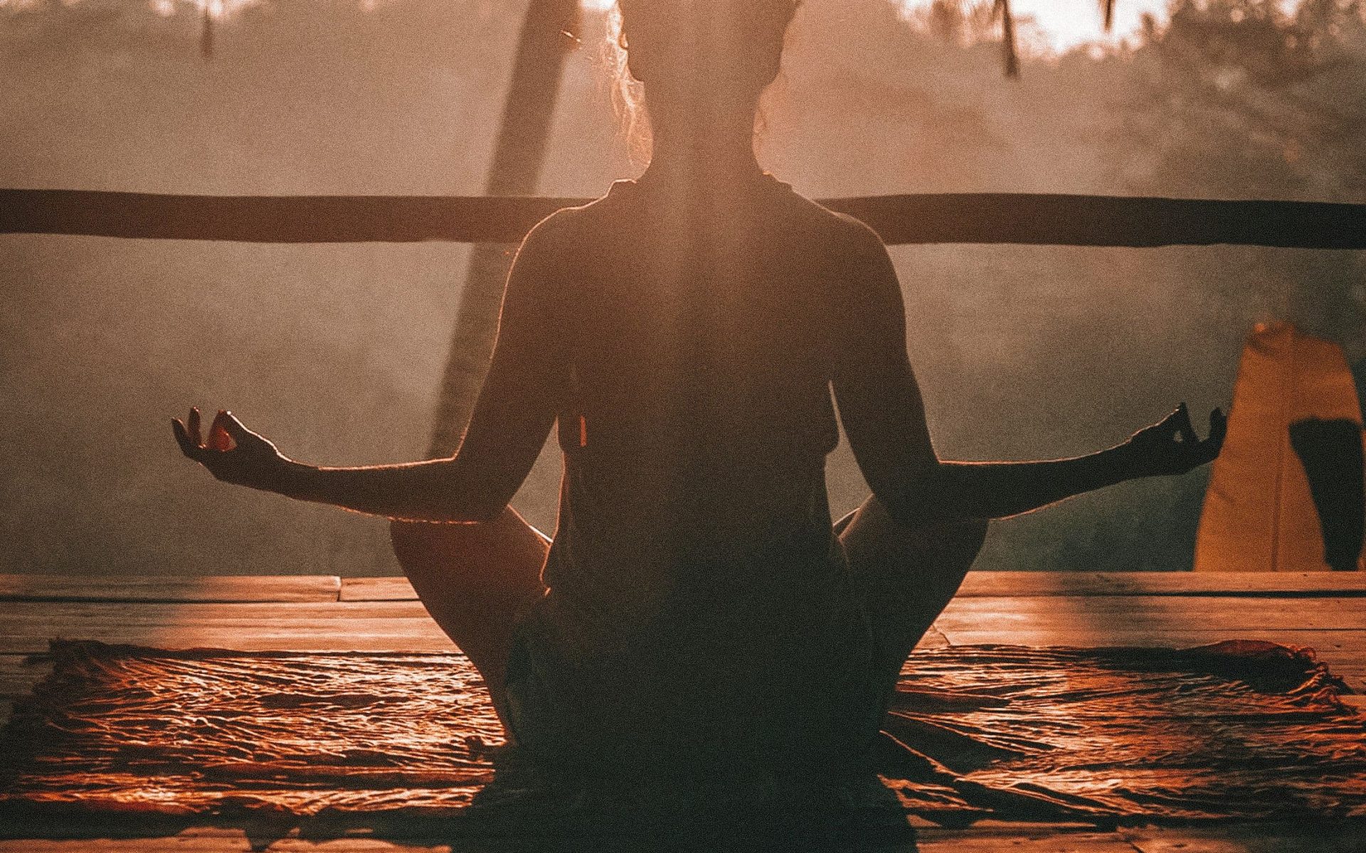 Person meditating at sunrise in a serene tropical setting