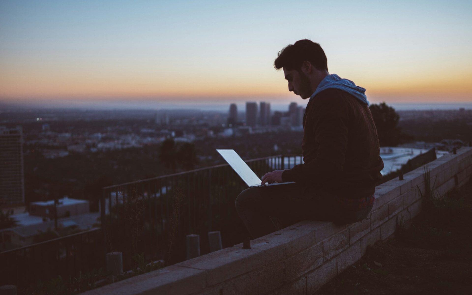Digital nomad working on a laptop with a cityscape at sunset in the background